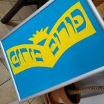 Na zdjęciu tablica z niebiesko-żółtym napisem po hebrajsku "Purim".